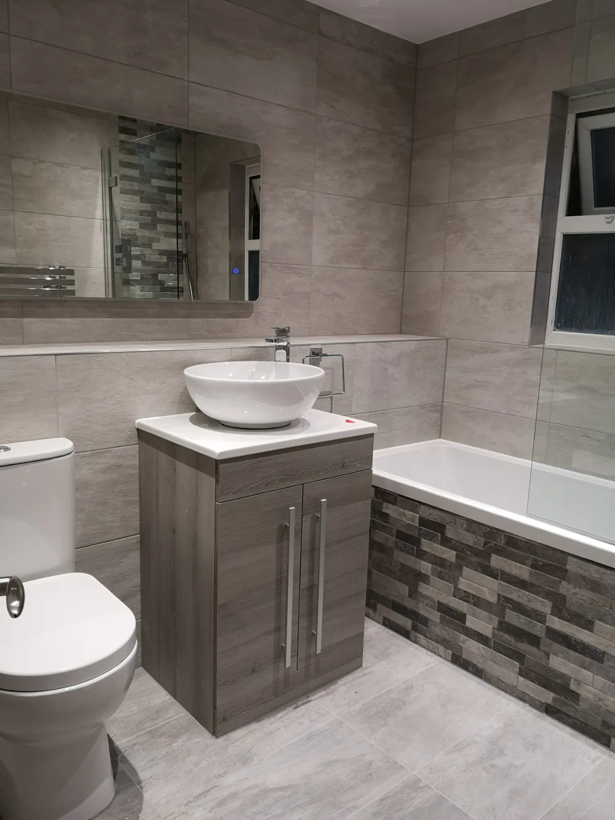 Grey bathroom refit with a panelled bath, mosaic feature tiling, vanity unit and WC by GJS in Essex