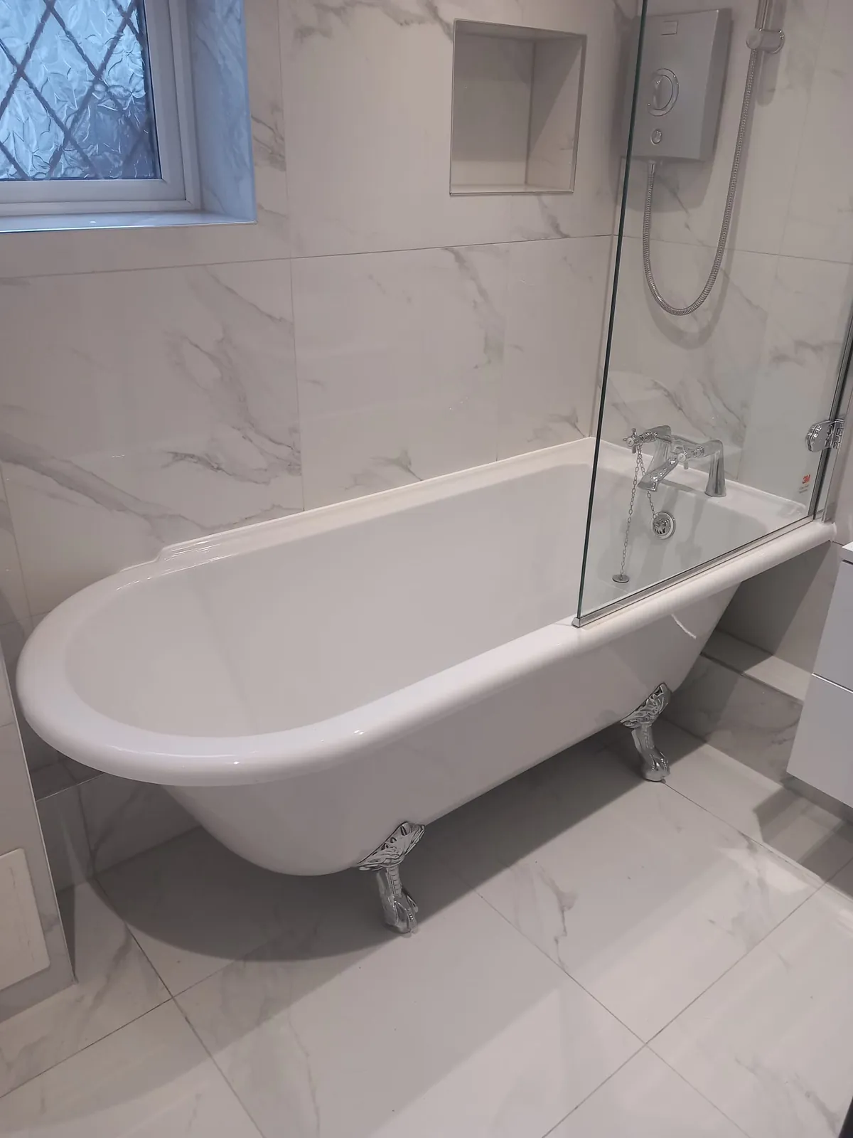 Freestanding roll-top bath with chrome feet in a white marble-effect bathroom by GJS in Essex