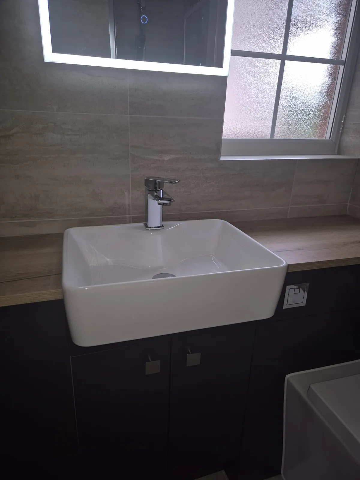 White countertop basin on a dark vanity unit with a chrome mixer tap, fitted by GJS in Essex