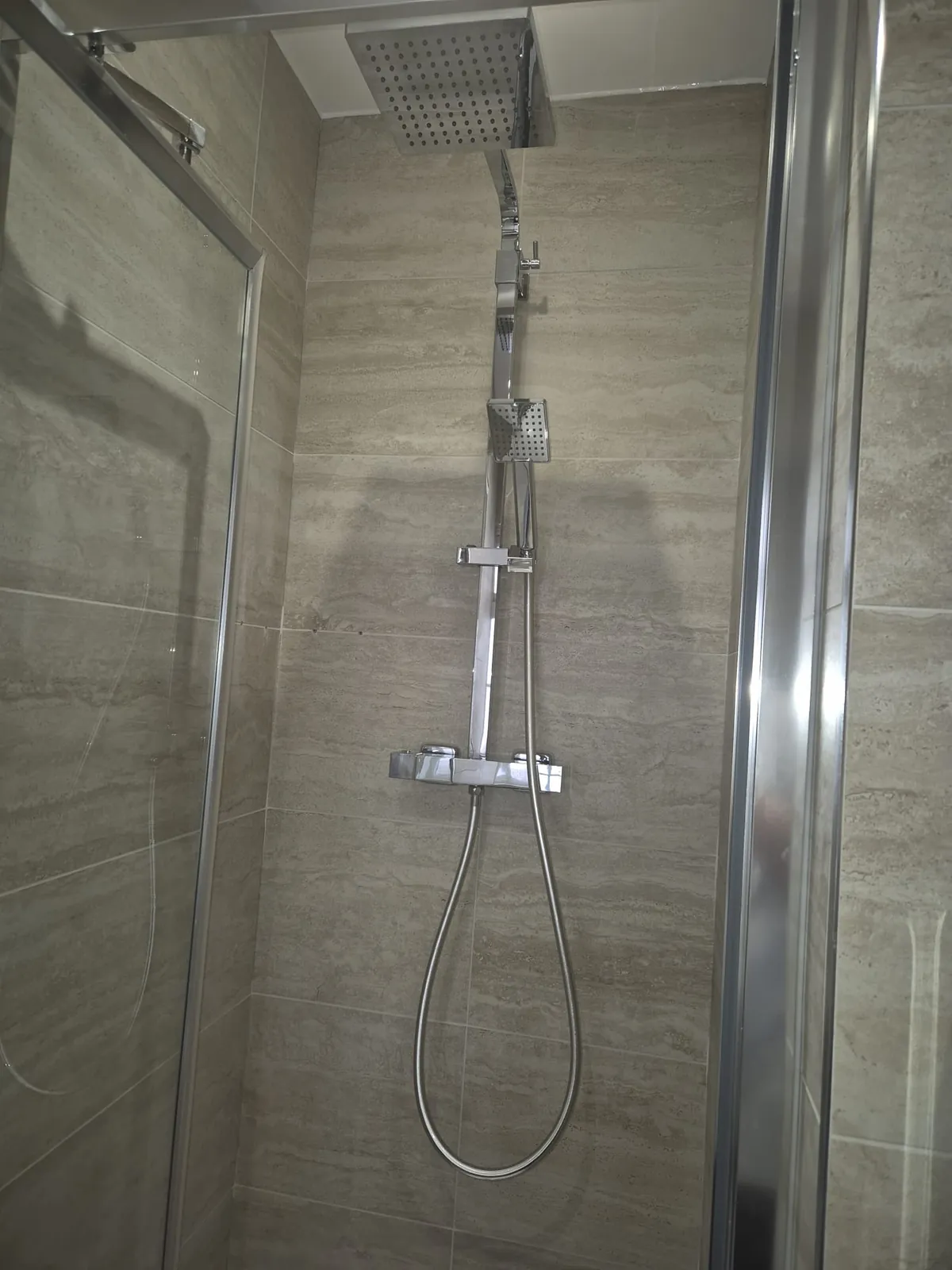Thermostatic shower with a rainfall head and handset in a tiled enclosure by GJS in Essex