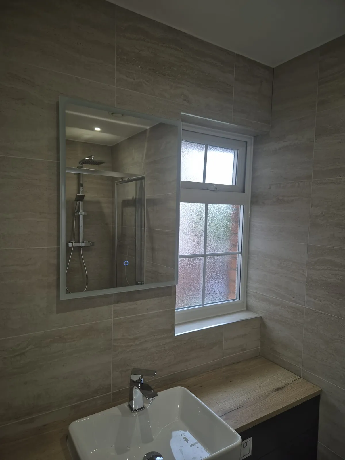 Mirrored bathroom cabinet above a basin with grey tiling, installed by GJS in Essex