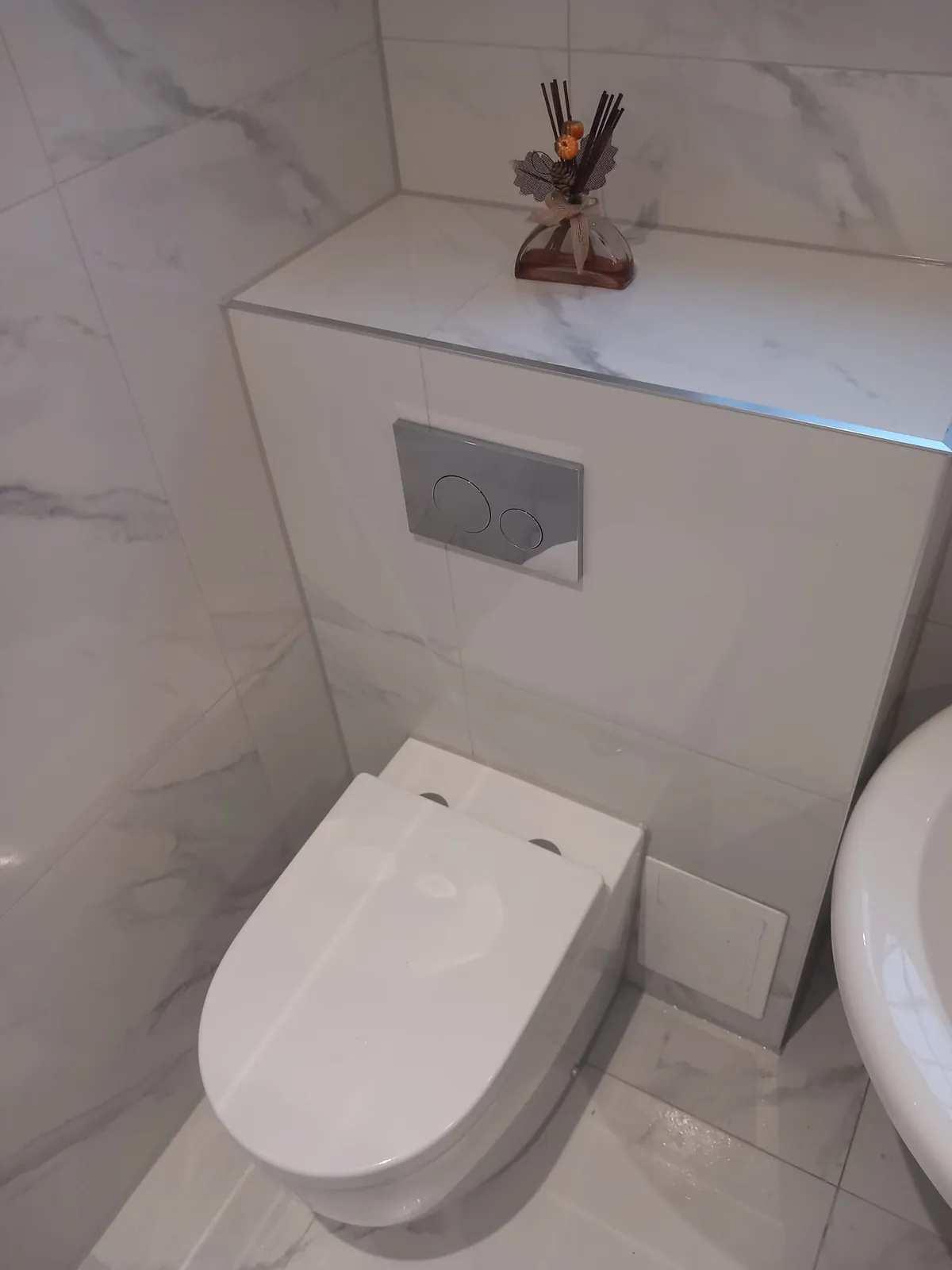 Wall-hung WC with a concealed cistern and chrome flush plate in a marble-effect bathroom by GJS